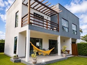 Ein modernes, zweistöckiges Haus mit Balkon, großen Fenstern und einer Hängematte.