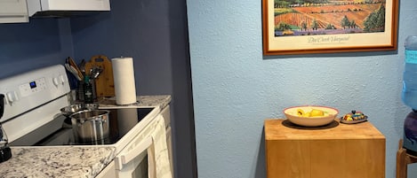 A kitchen with white cabinets, a microwave, a stove, and a wooden table with a bowl of fruit.
