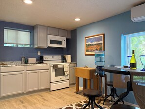 A kitchen with white cabinets, a microwave, a stove, and a water dispenser. - Cozy studio apartment in beautiful Guerneville with AC overlooking the creek (Guerneville)