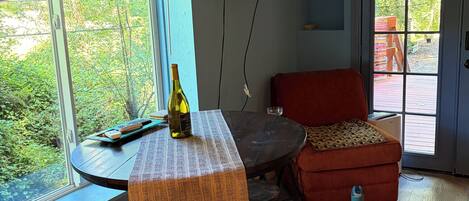 A room with a dining table, a red sofa, a TV mounted on the wall, and a window with a view of greenery.