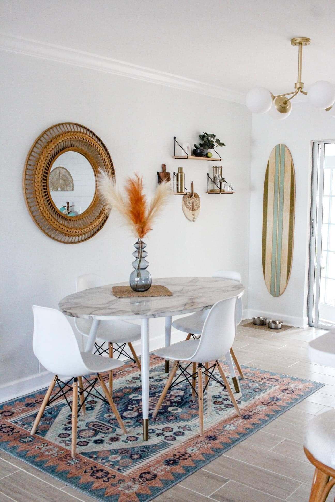 Un coin repas avec une table ronde, des chaises blanches, un tapis à motifs et une décoration murale représentant une planche de surf.