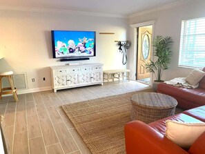 A living room with a flat-screen TV, a white cabinet, a wicker ottoman, a red sofa, and a large woven rug. - Bonita Shores Beach House Close to Doc's, Barefoot Beach, Naples +Dog-Friendly! (Bonita Springs)