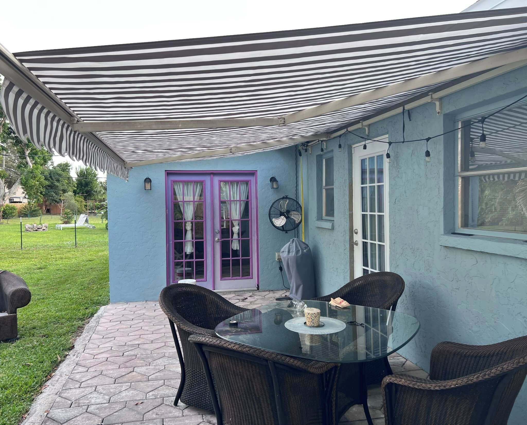 A patio area with a glass table and wicker chairs, a purple door, and a fan.