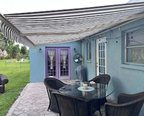A patio area with a glass table and wicker chairs, a purple door, and a fan. - Bonita Shores Beach House Close to Doc's, Barefoot Beach, Naples +Dog-Friendly! (Bonita Springs)
