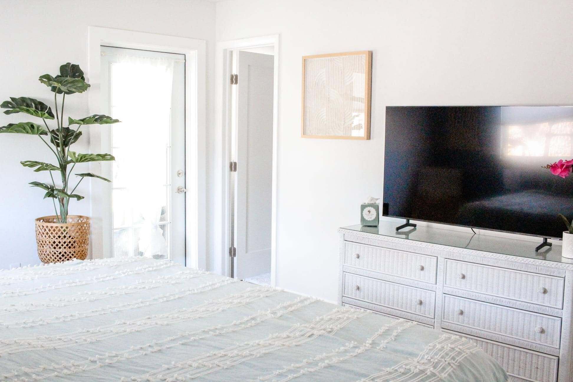 A room with a television on a white dresser, a plant, and a door leading to another room.