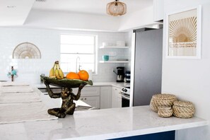 A kitchen with a marble countertop, a hanging light fixture, a framed artwork, and wicker baskets. - Bonita Shores Beach House Close to Doc's, Barefoot Beach, Naples +Dog-Friendly! (Bonita Springs)