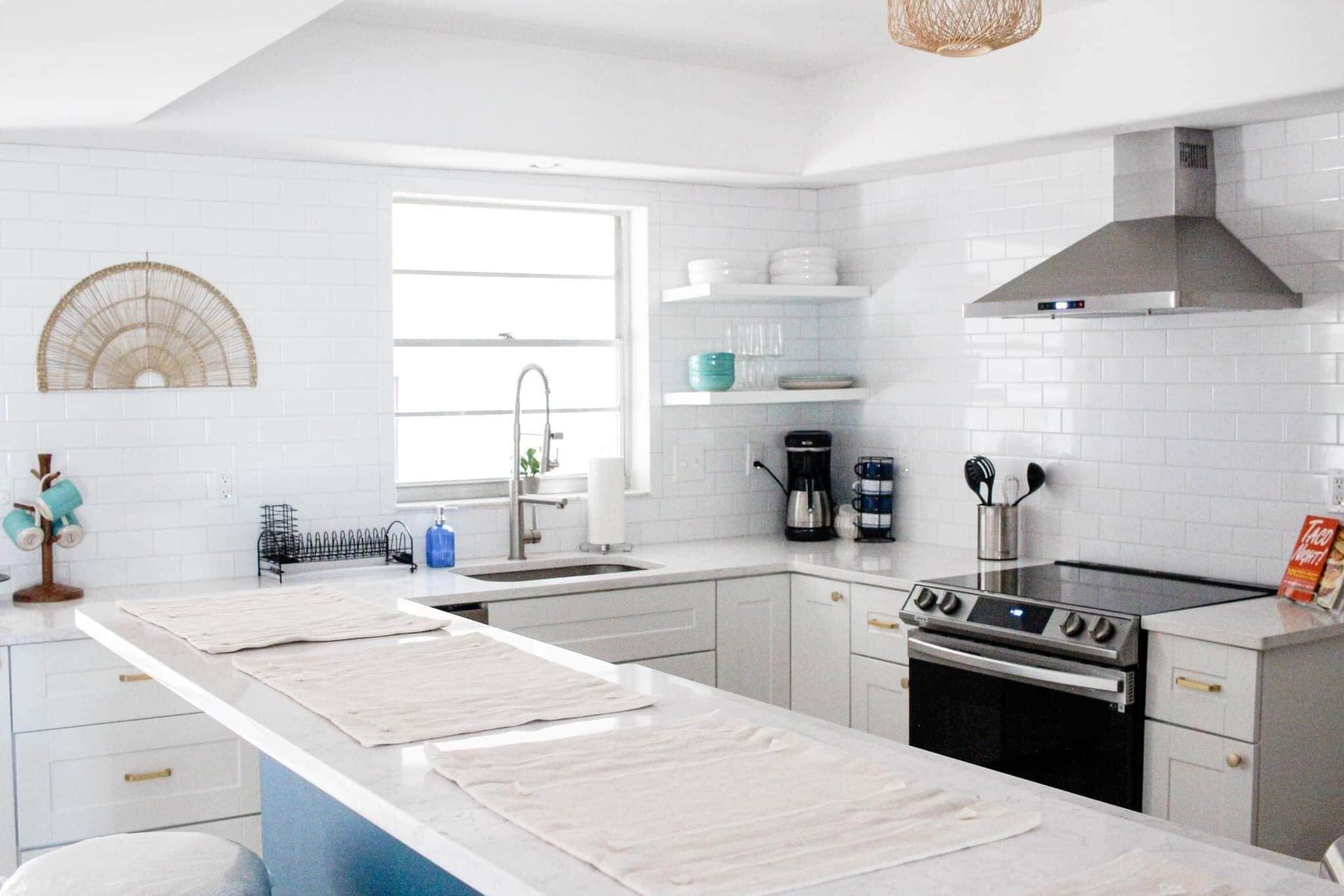 A modern kitchen with white cabinetry, a central island, a stove, and a coffee maker.