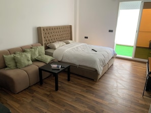 Ein Schlafzimmer mit einem Bett, einem Schlafsofa, einem kleinen Tisch und einer Glasschiebetür, die auf einen Balkon führt.