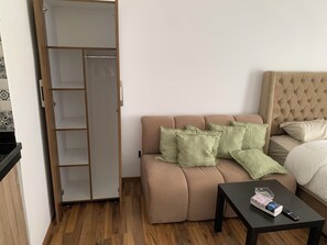 Ein Zimmer mit einem beigefarbenen Sofa, einem Bett mit gestepptem Kopfteil, Holzboden und einem schwarzen Tisch mit Fernbedienung.