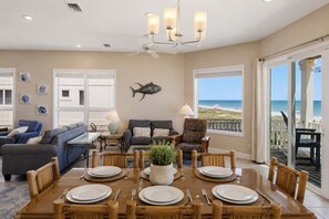 A dining area with a wooden table set for six, surrounded by bamboo chairs, a sofa, and a patterned armchair. - Sea Forever SGI Beach Front 5 Bedroom  Hot tub Pool (Saint George Island)