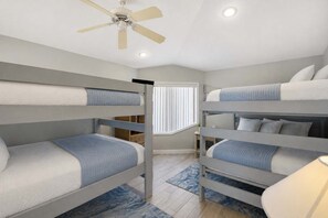 A room with bunk beds, a ceiling fan, a window with blinds, and a blue patterned rug.