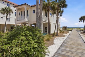 Une propriété située en bord de mer, avec une promenade en bois menant à un bâtiment doté de nombreux balcons et d’un espace piscine.