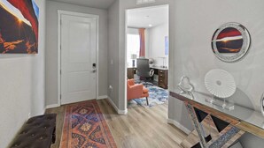 A hallway with a door, a patterned rug, a desk with a fan, and a wall with a framed picture. - Spacious 3-bedroom house with AC in welcoming Colorado Springs (Colorado Springs)
