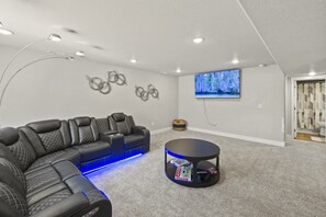 Une salle de divertissement équipée d’un canapé d’angle, d’une table basse ronde et d’un téléviseur à écran plat fixé au mur.