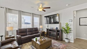 A living room with a brown leather sofa, a wooden coffee table, a fireplace, and a television mounted on the wall. - Spacious 3-bedroom house with AC in welcoming Colorado Springs (Colorado Springs)