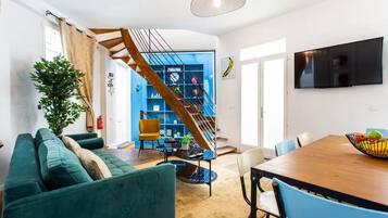 A modern living room with a teal sofa, a wooden dining table, and a staircase leading to a blue room.
