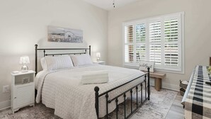 Quarto com cama, ventoinha no teto, janela com cortinas e mesas de cabeceira.