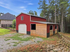 A red barn with a white garage door, wooden siding, and a gravel driveway. - Big Ridge Hideaway - Hot Tub (Talking Rock)
