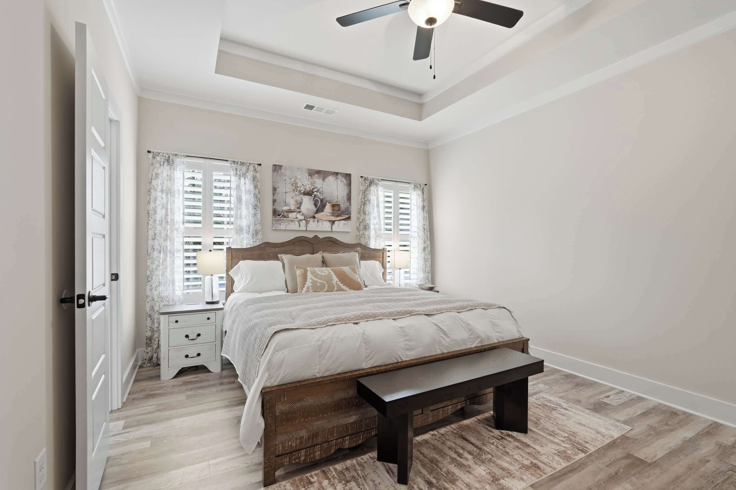 A bedroom with a bed, a bench, a nightstand, and a ceiling fan.