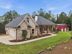 A two-story house with a stone facade, a covered porch, and a red barn in the background. - Big Ridge Hideaway - Hot Tub (Talking Rock)