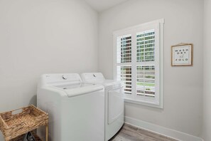 A laundry room with two white front-loading washing machines, a wicker basket, and a window with white shutters. - Big Ridge Hideaway - Hot Tub (Talking Rock)