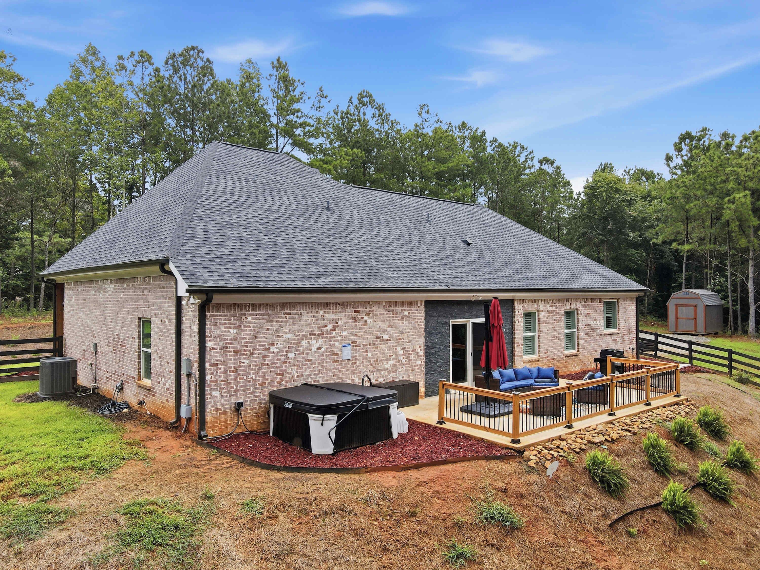 A single-story brick house with a covered patio area, a hot tub, and a fenced yard.