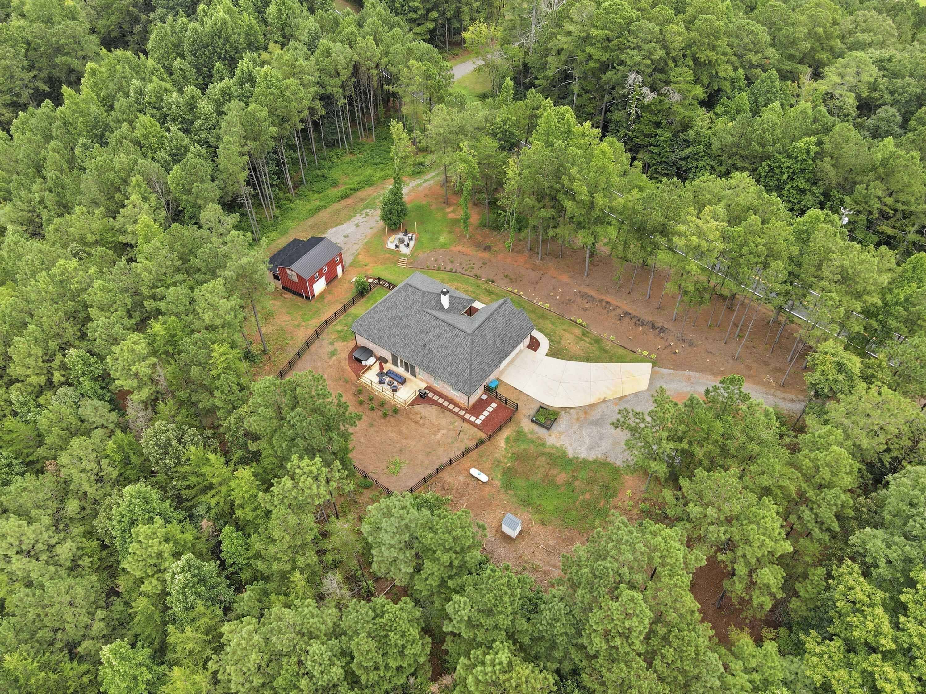 A house surrounded by dense forest, with a large driveway and a covered outdoor area.