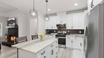 Cocina moderna con gabinetes blancos, una isla central, horno empotrado y refrigerador de acero inoxidable.