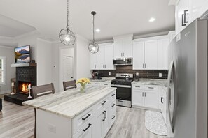 Cocina moderna con gabinetes blancos, una isla central, horno empotrado y refrigerador de acero inoxidable.