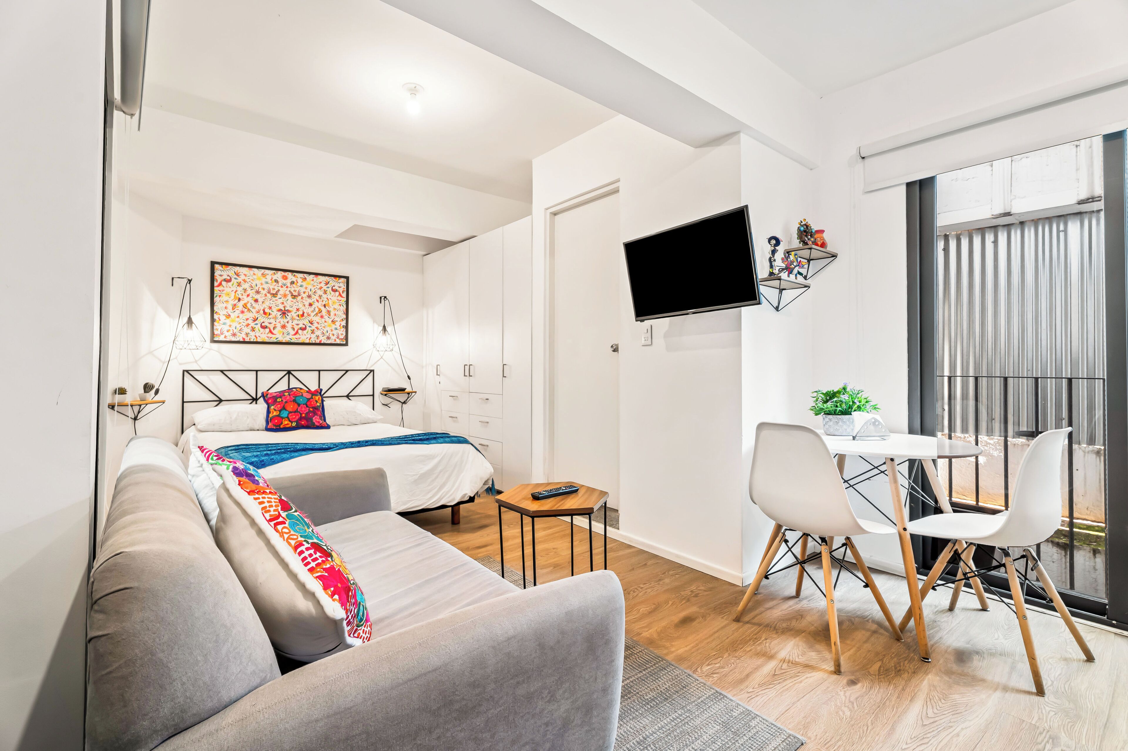 A modern hotel room with a bed, a sofa, a desk, and a TV.