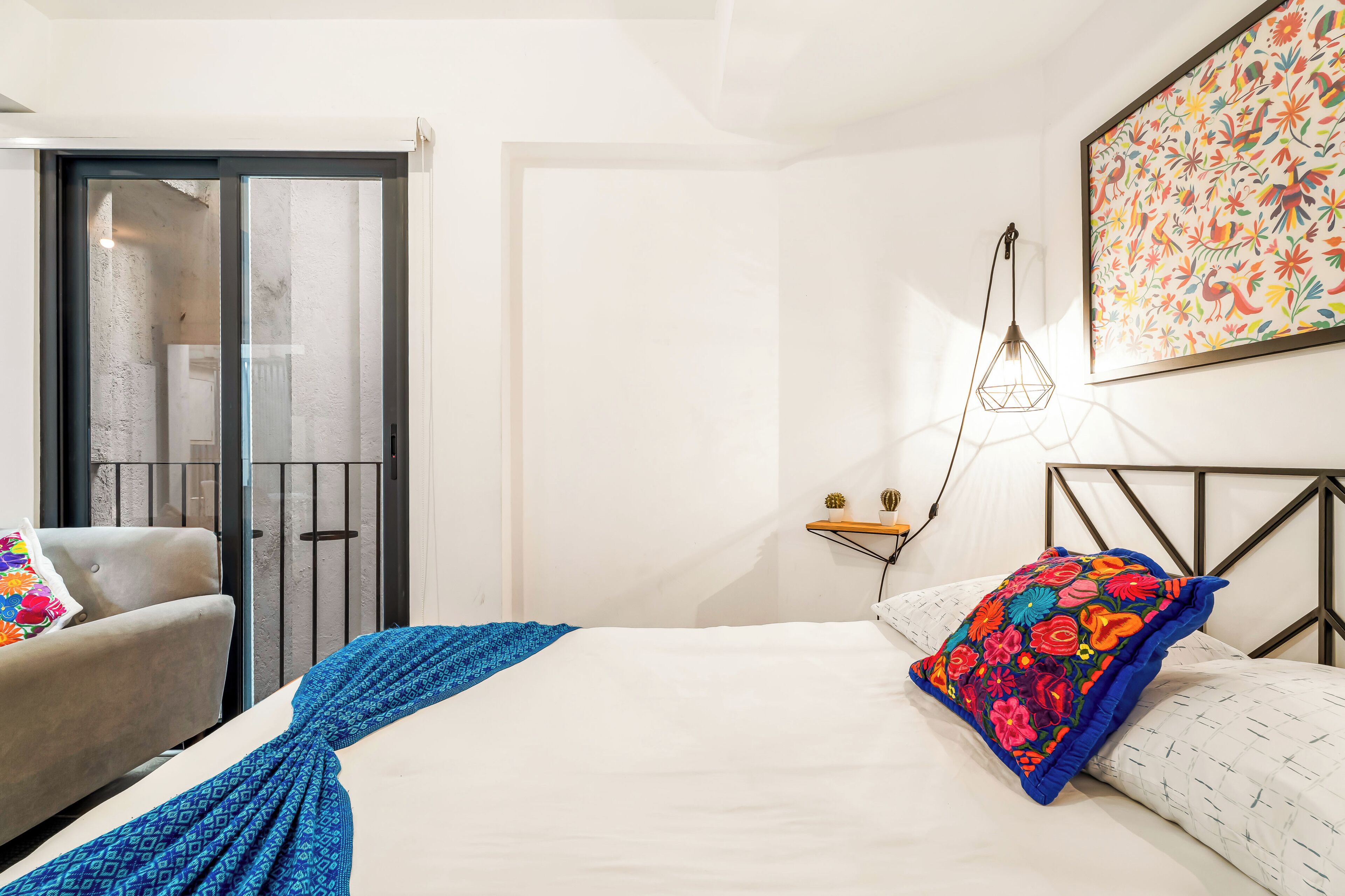A bedroom with a bed, a chair, a wall-mounted shelf, and a door leading to a balcony.