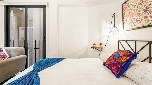 A bedroom with a bed, a chair, a wall-mounted shelf, and a door leading to a balcony. - Loft in the Historic Center of the City (Ciudad de México)