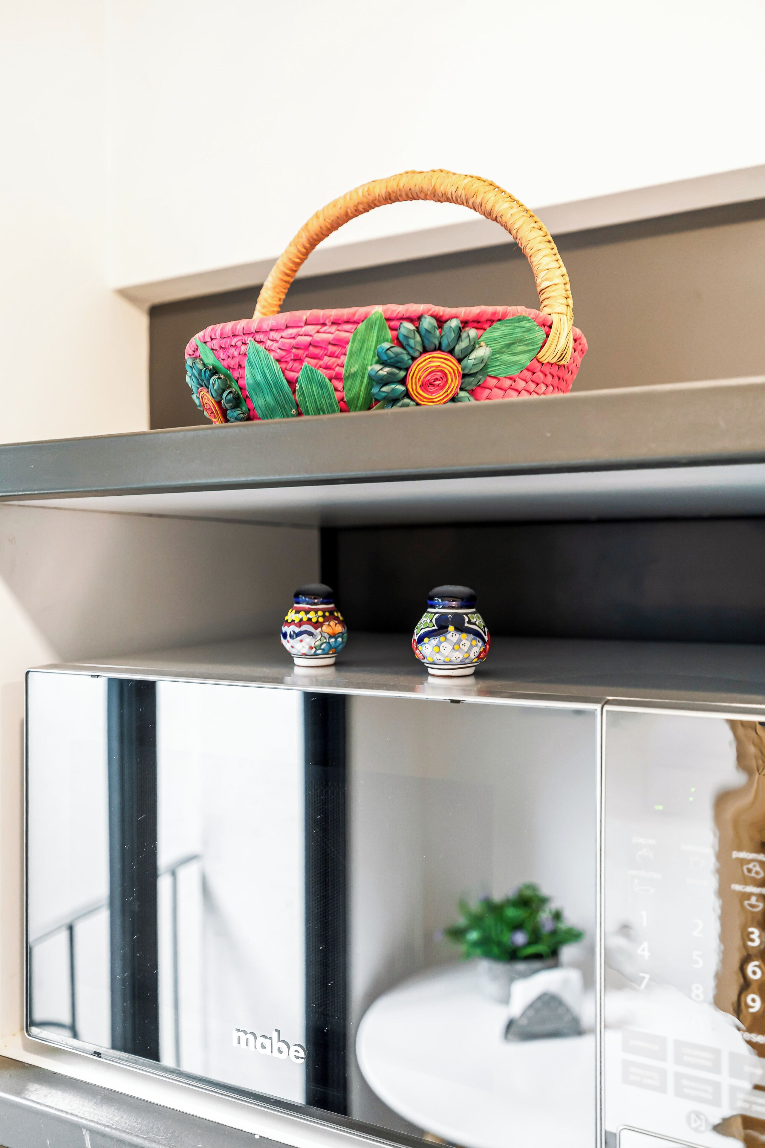 A shelf with a woven basket, two decorative vases, and a mirrored cabinet.