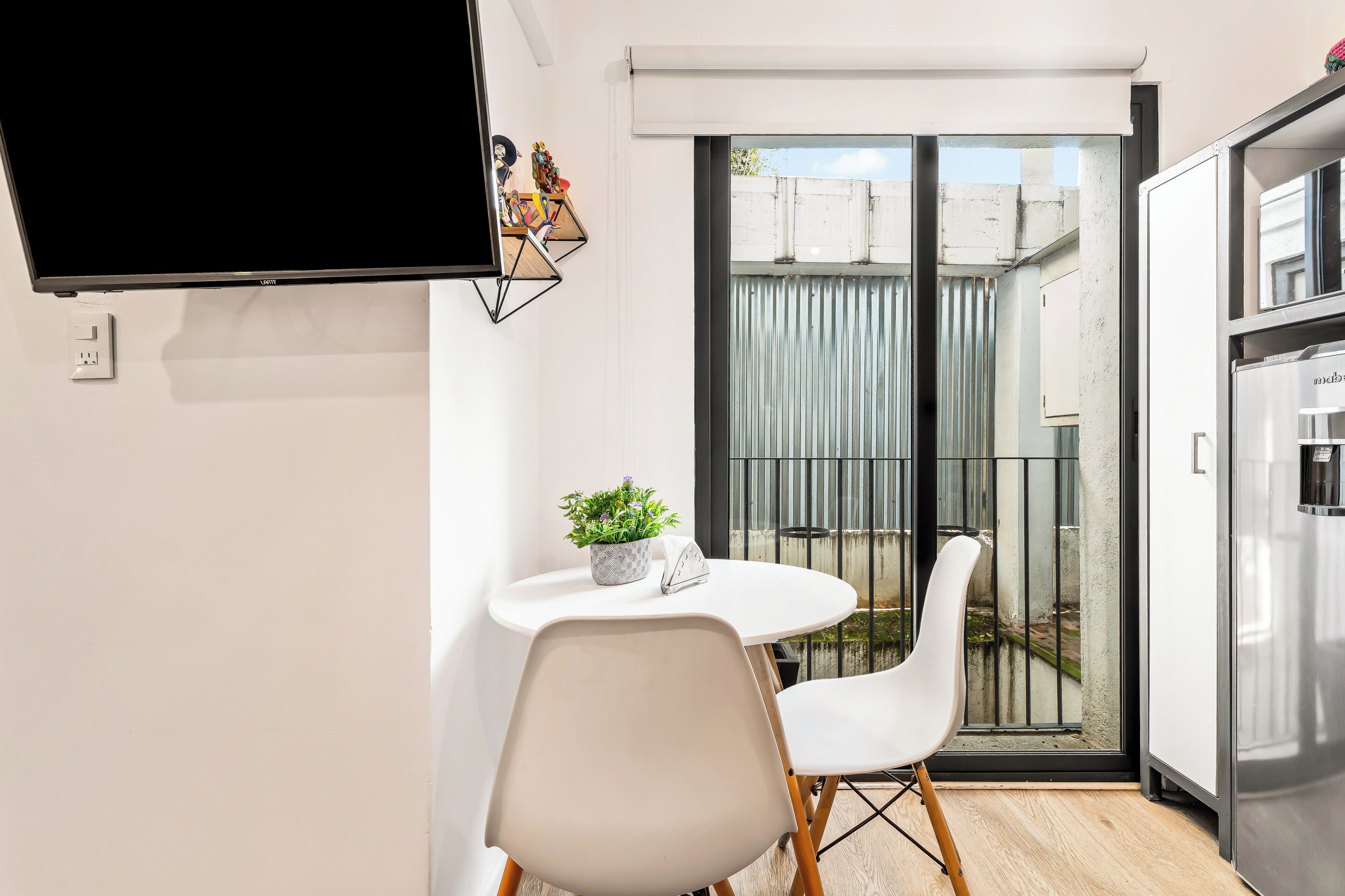 A modern kitchen with a built-in refrigerator, a dining table with chairs, and a TV mounted on the wall.