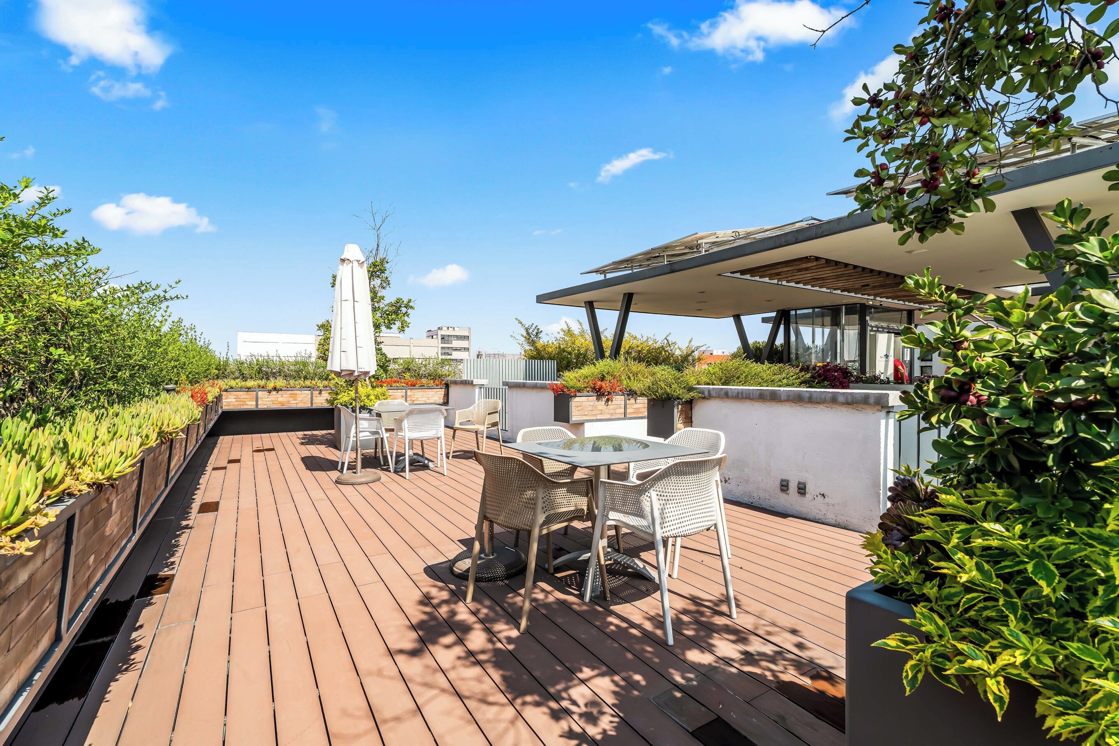 A rooftop terrace with a wooden deck, outdoor seating, and a view of the city skyline.
