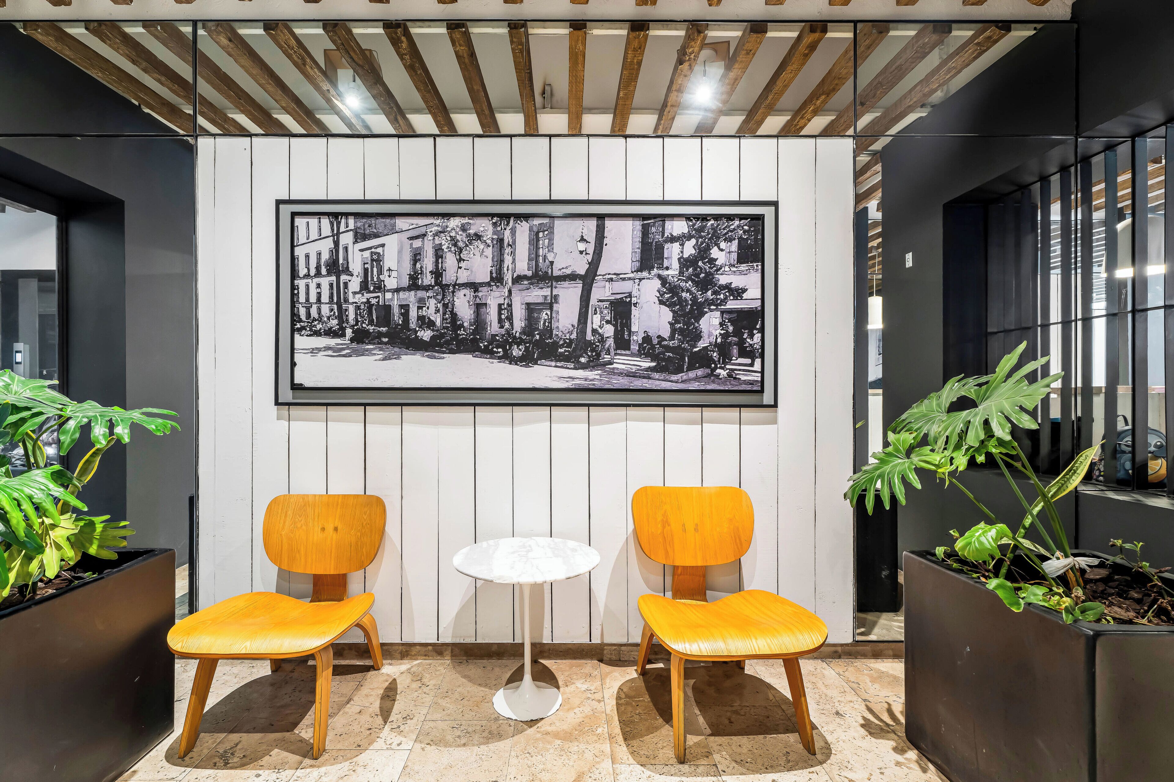 A modern interior with two wooden chairs, a small white table, and a large framed black and white photograph on the wall.