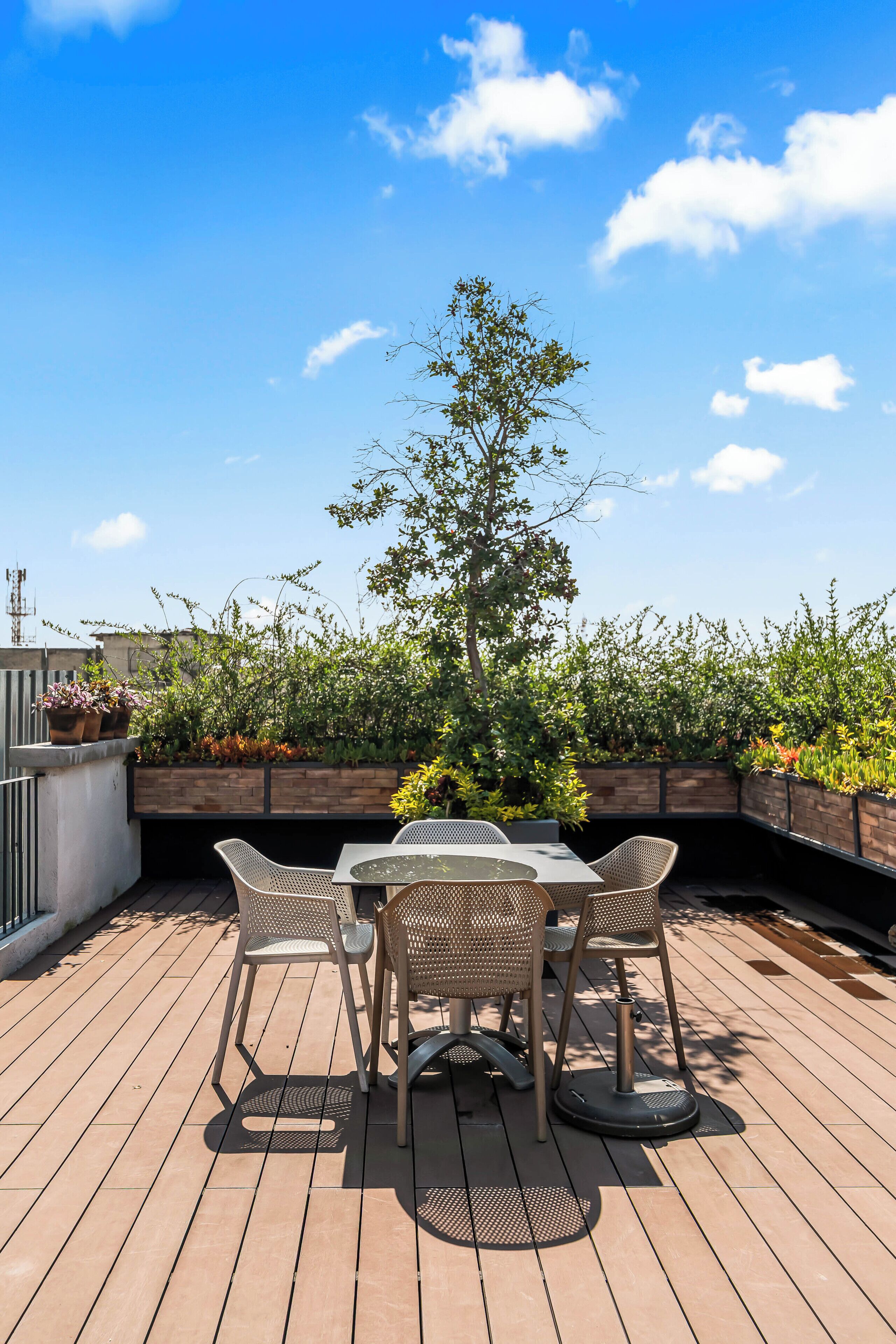 An outdoor patio with a table and chairs, surrounded by greenery and a clear sky.