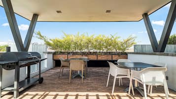 An outdoor patio with a grill, seating area, and a view of trees.