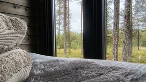 A bed with a grey blanket and a view of a forest through a window.