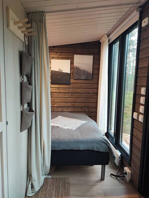 A bedroom with a bed, a window, wooden walls, and a view of the outdoors.