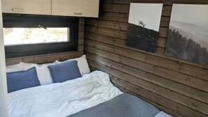 A bedroom with a bed, pillows, a window, wooden walls, and artwork.