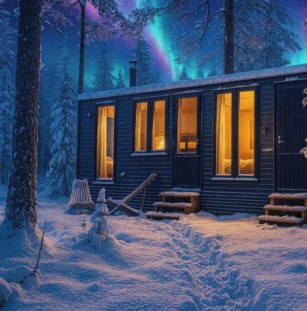 Una cabaña con múltiples ventanas, suelo cubierto de nieve y un fondo arbolado.