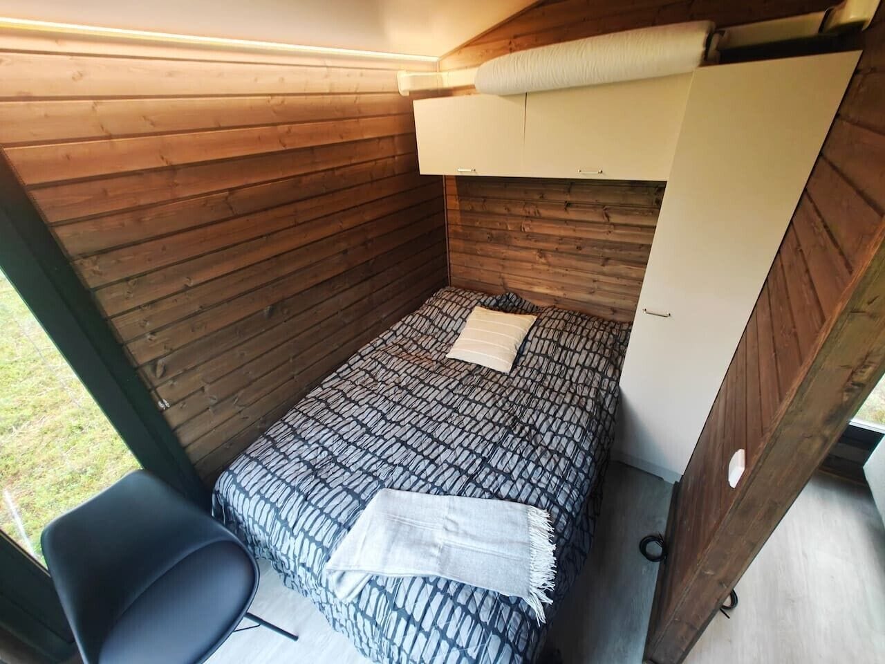 A small, enclosed room with a bunk bed, a single chair, and a window.