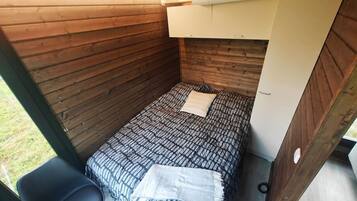A small, enclosed room with a bunk bed, a single chair, and a window.