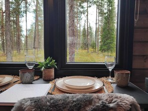 Una mesa lista con platos, vasos y un menú, con vista a un bosque a través de una ventana.