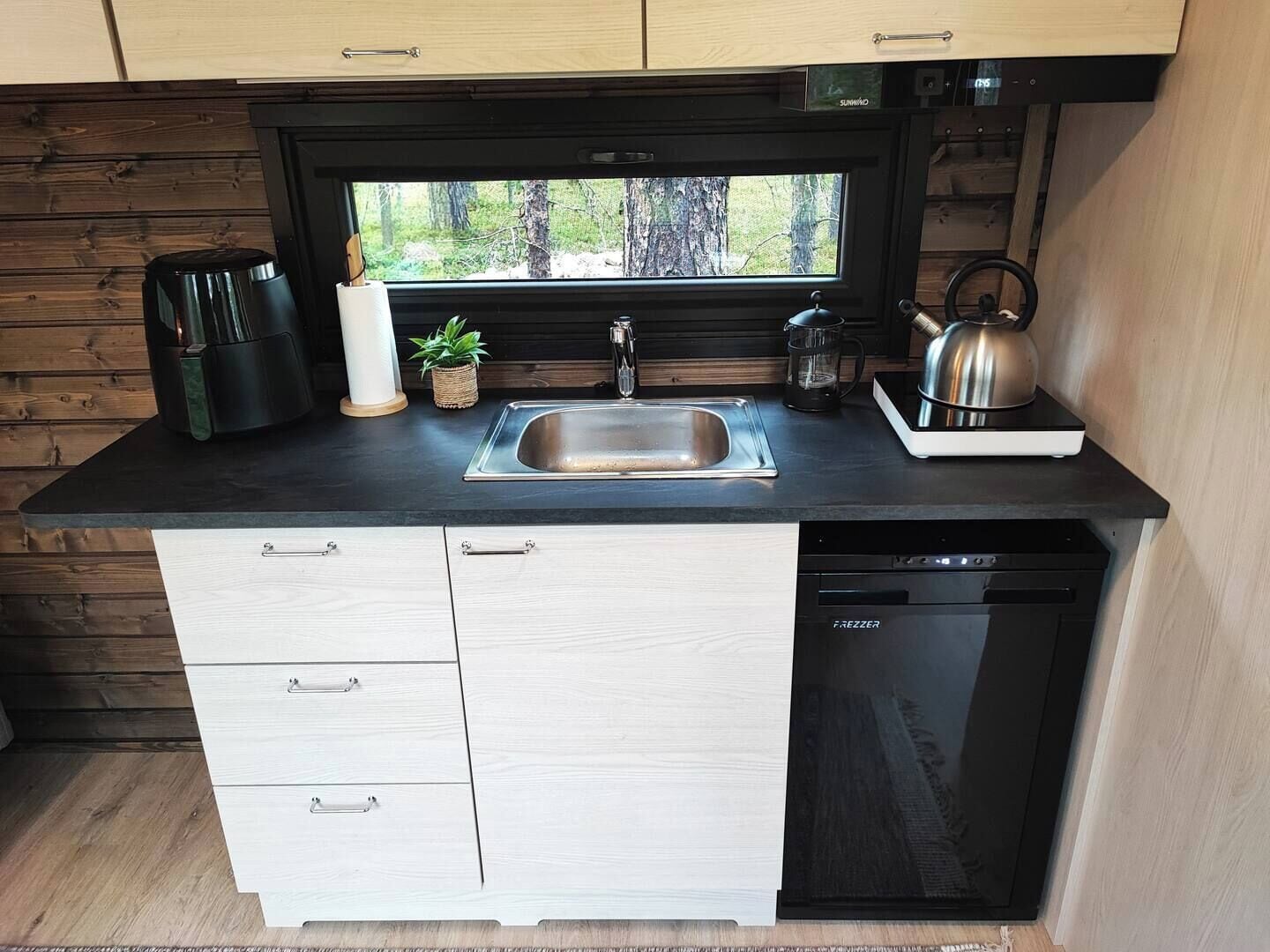 A compact kitchen with a sink, a kettle, a coffee maker, and a dishwasher.