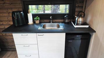A compact kitchen with a sink, a kettle, a coffee maker, and a dishwasher.