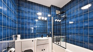 Une salle de bain avec des carreaux bleus, un lavabo blanc, des toilettes et un espace douche.