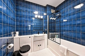 Ein Badezimmer mit blauen Fliesen, einem weißen Waschbecken, einer Toilette und einer Duschkabine.