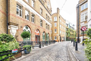 Eine gepflasterte Straße, gesäumt von Backsteingebäuden, von denen einige Rundbogenfenster und Schilder mit dem Schriftzug 'Bubala' aufweisen.